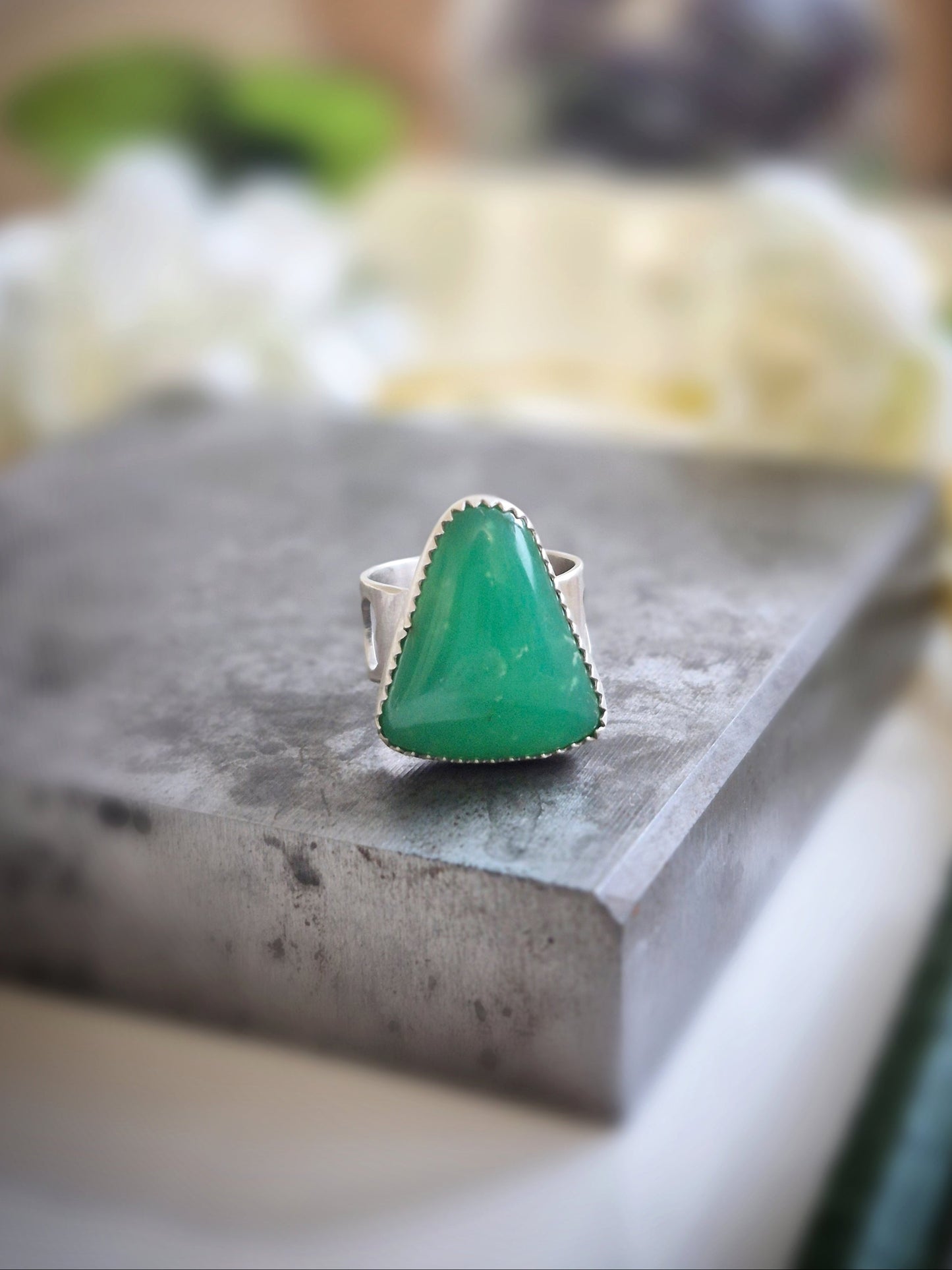 Green chrysoprase gemstone ring on a gray surface with a blurred background