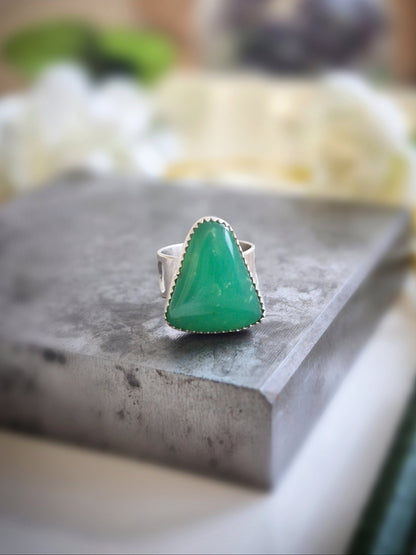 Green chrysoprase gemstone ring on a gray surface with a blurred background