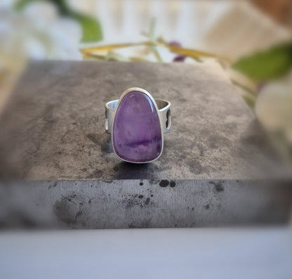 Silver ring with a purple amethyst stone on a gray surface with flowers in the background