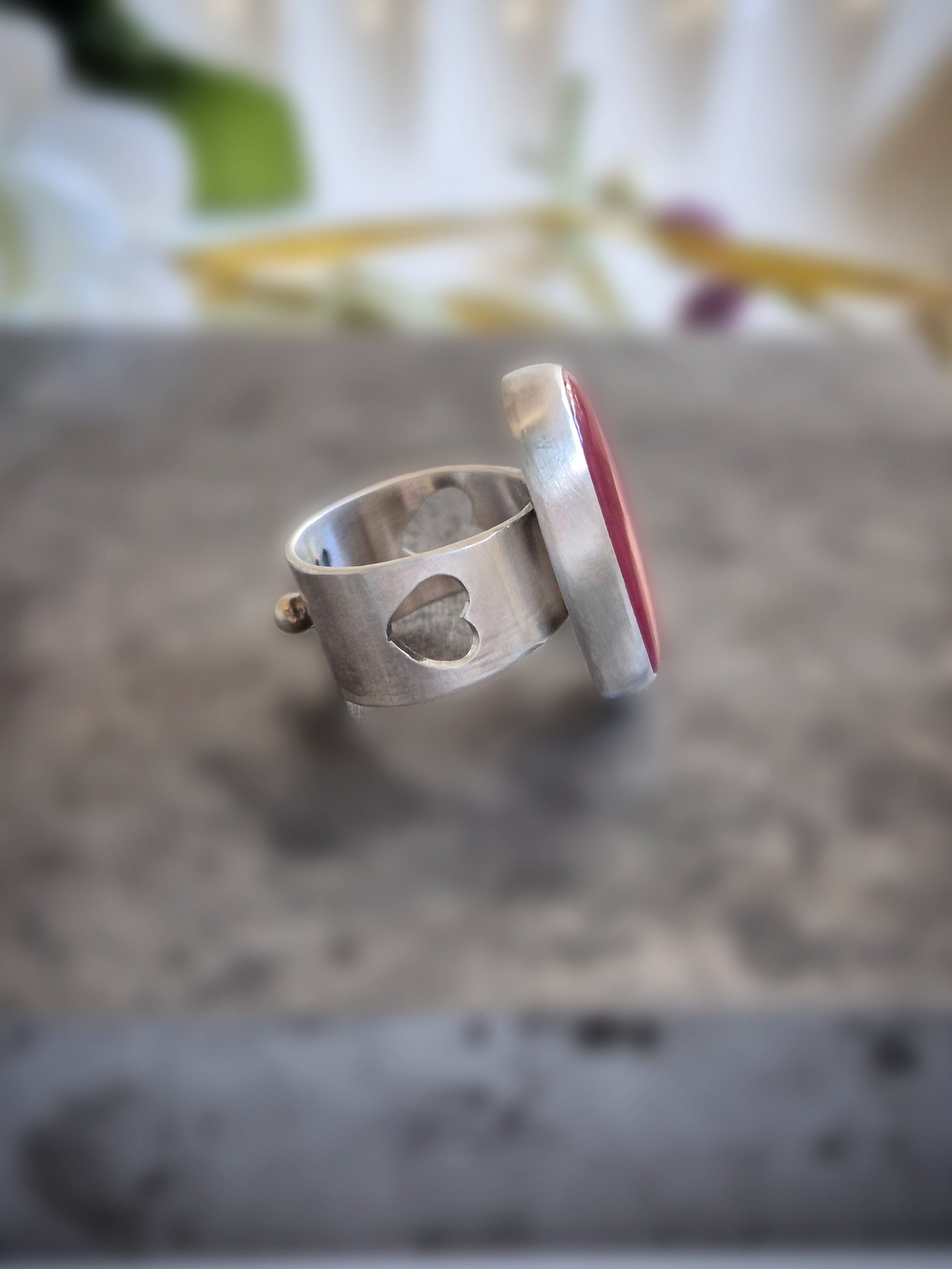 Silver ring with a red rosarita stone on a textured surface