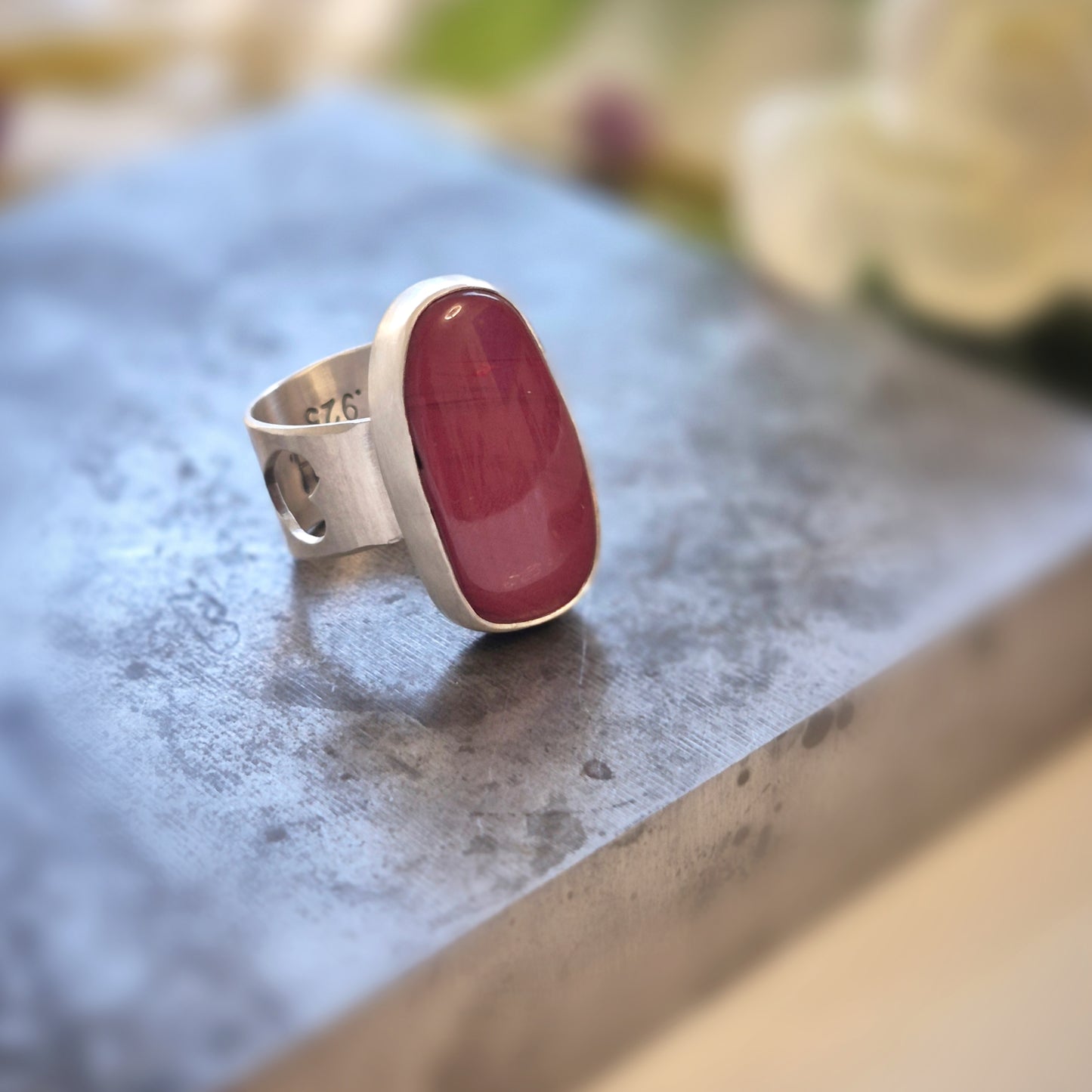 Silver ring with a red rosarita stone on a textured surface