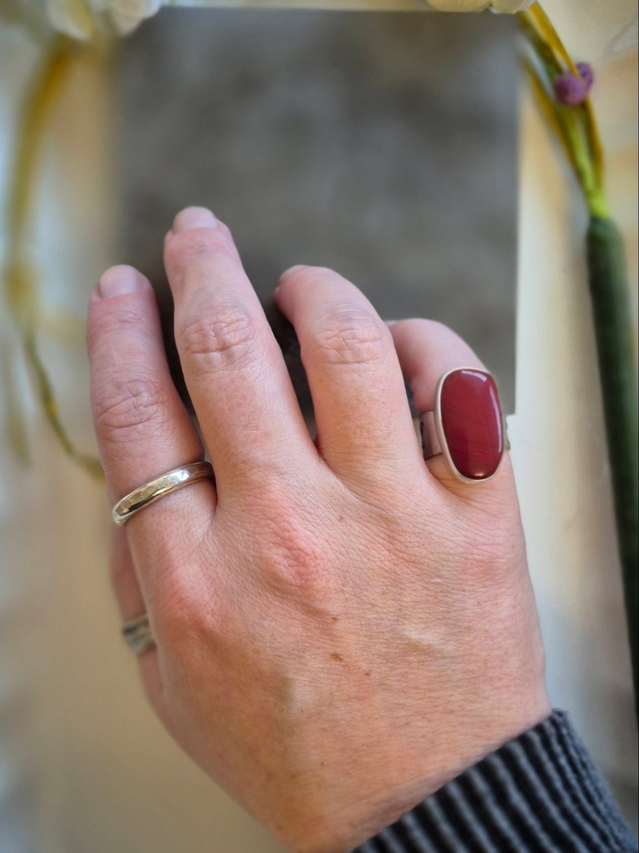 Hand wearing a red rosarita ring with a blurred mirror and flowers in the background