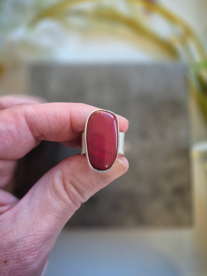 Ring with a red rosarita stone held by a hand against a blurred background