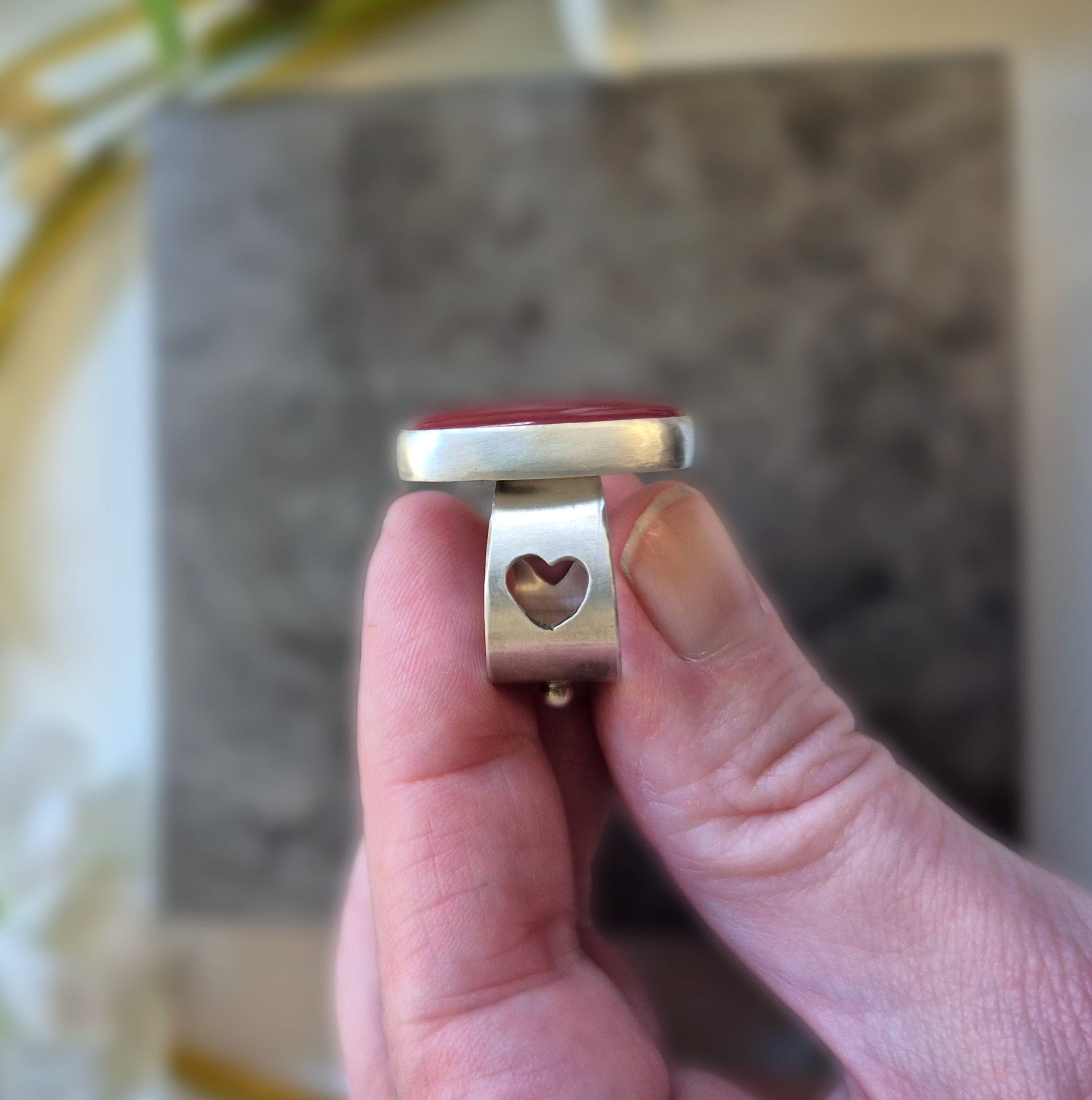 Gold ring with a heart design held by a hand against a blurred background