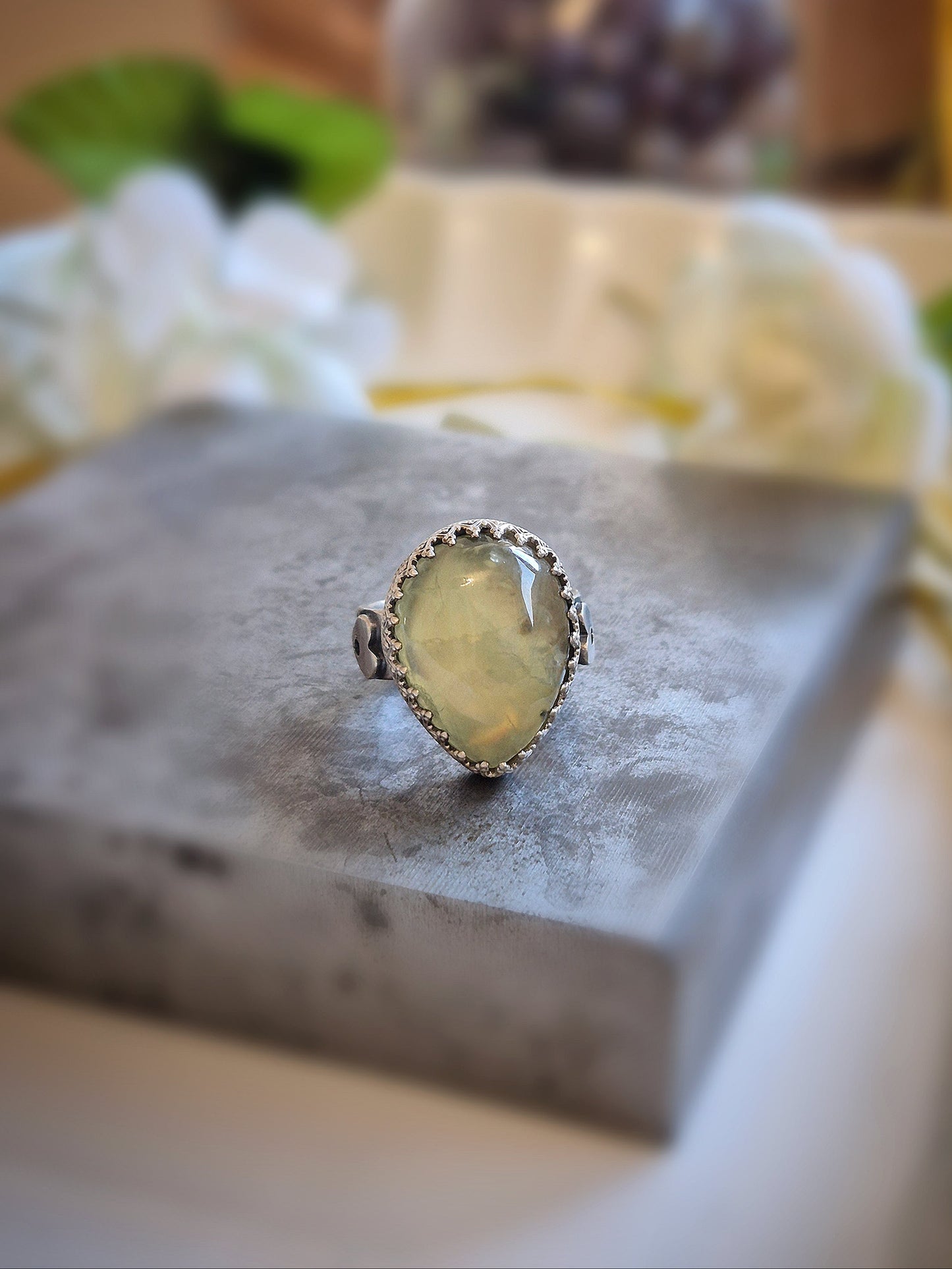 Ring with a yellow prehnite gemstone on a gray stone surface with blurred background