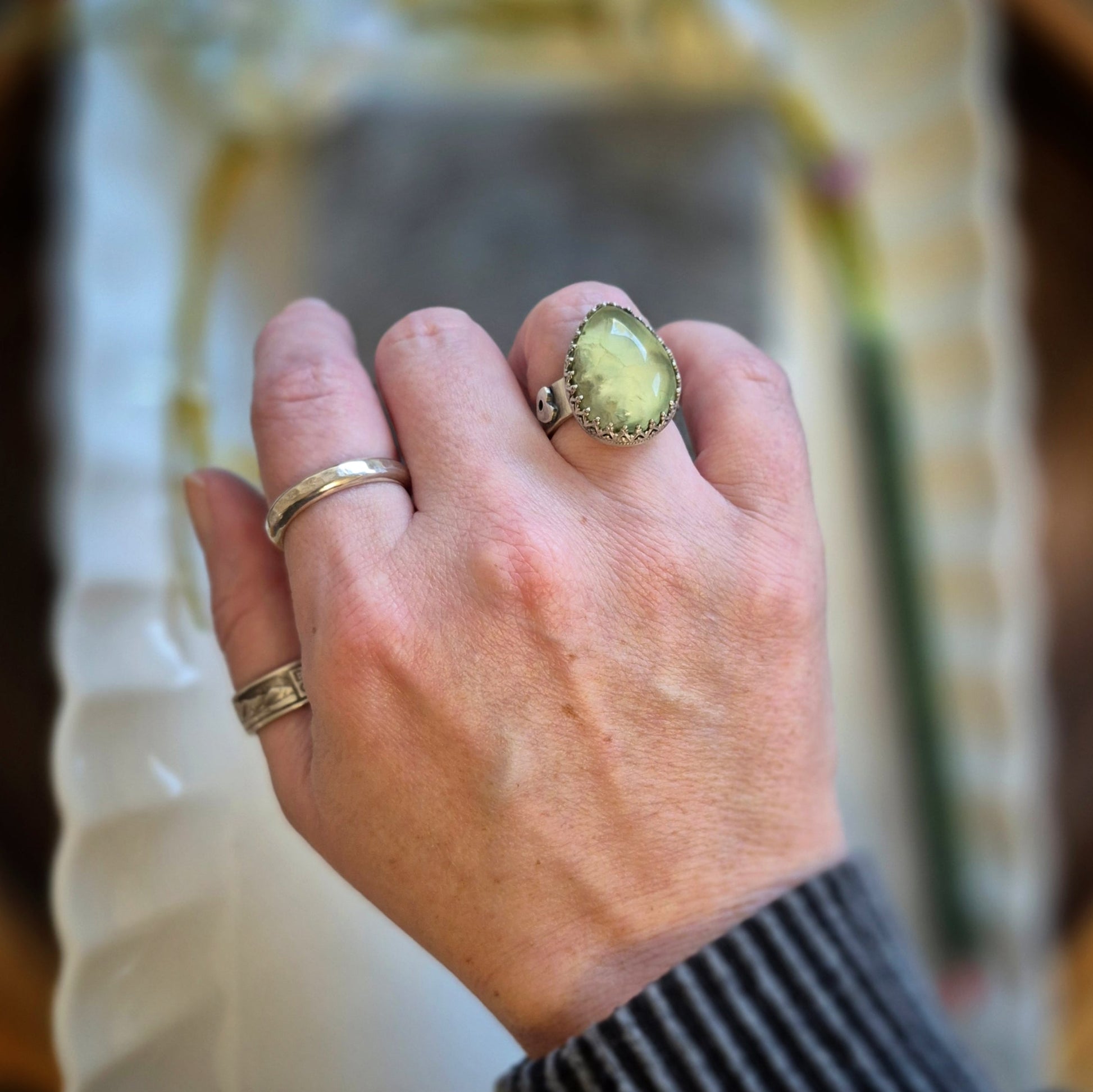 Hand wearing two rings with a yellow prehnite stone against a blurred background