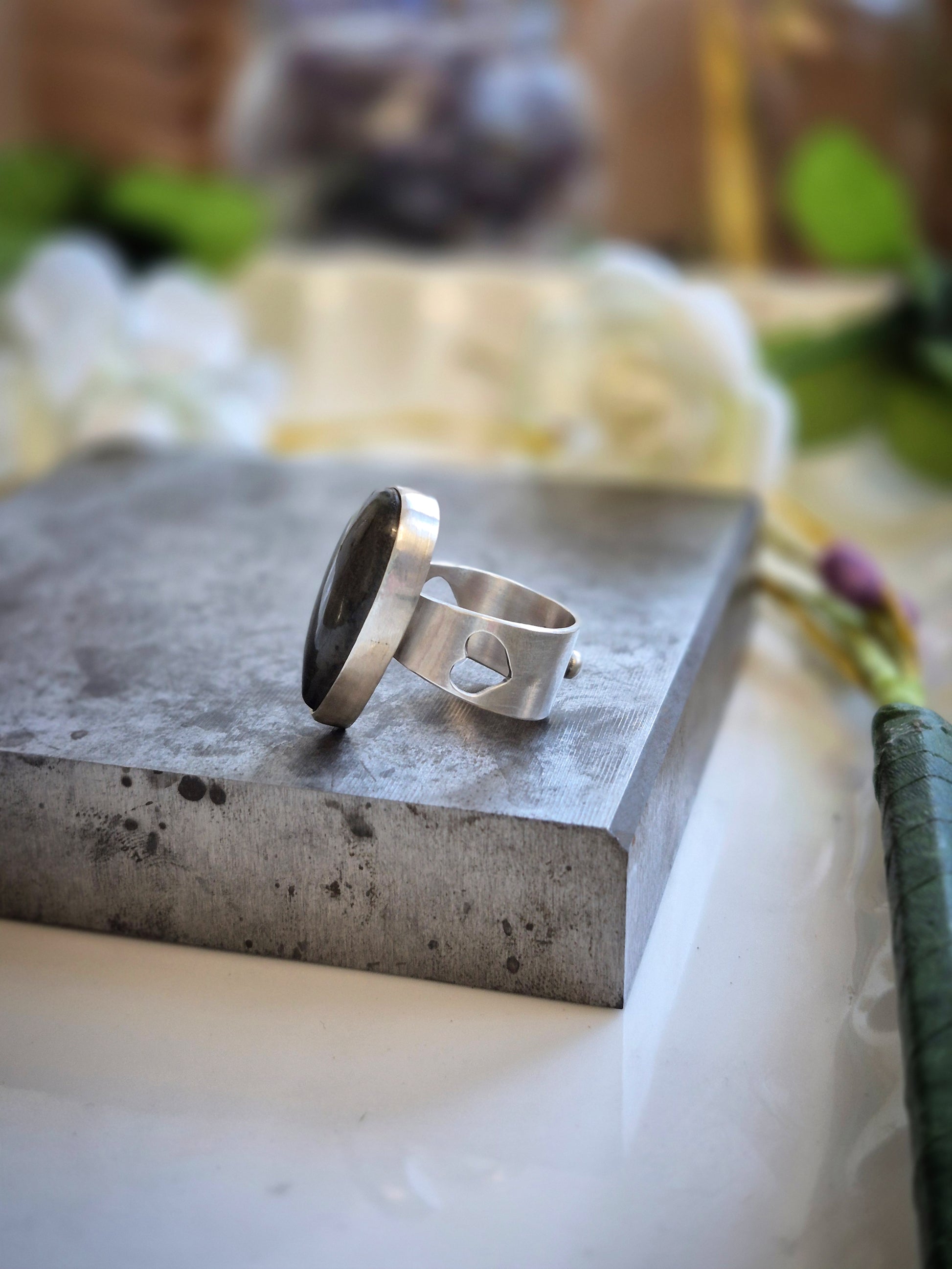 Silver labradorite ring on a concrete surface with a blurred natural background