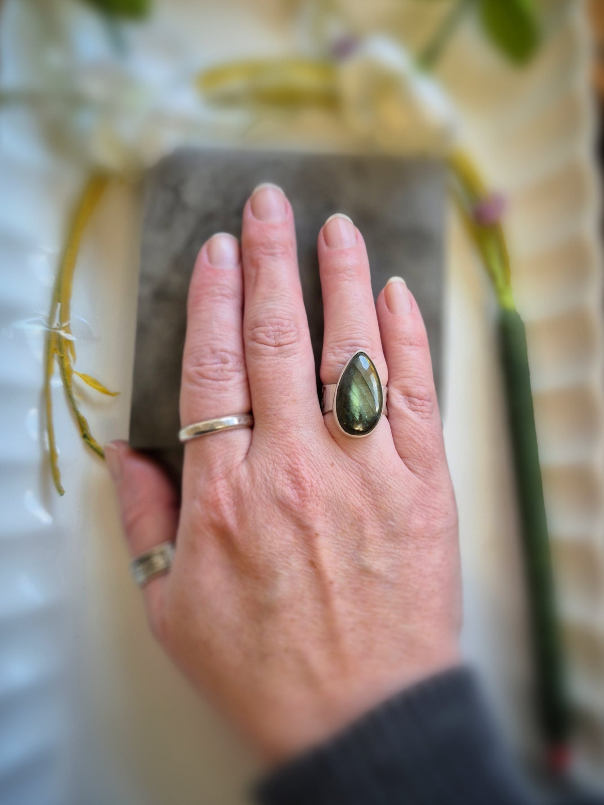 Hand wearing a ring with a green labradorite stone on a blurred background