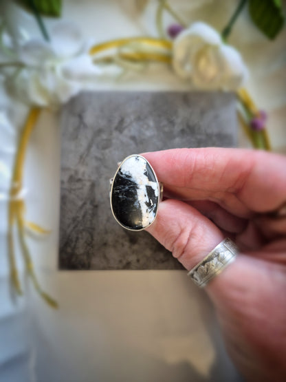 Hand holding a silver ring with a white buffalo stone against a neutral background