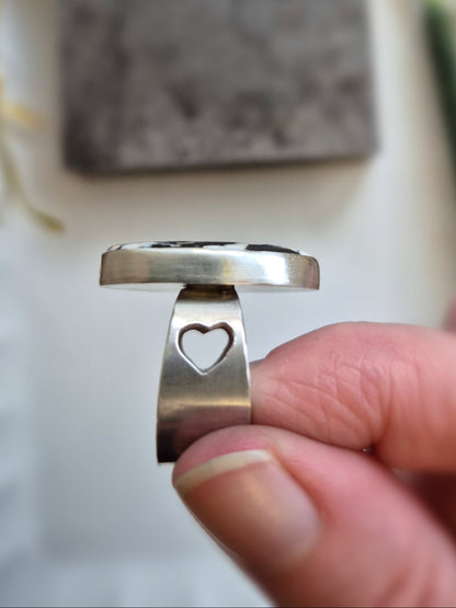 Silver ring with a heart cutout held by a hand, blurred background