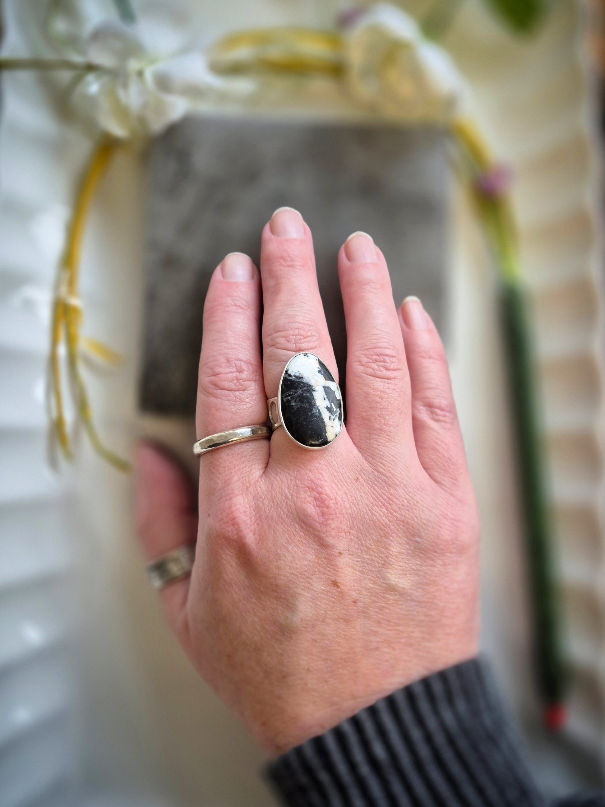 Hand wearing a ring with a white buffalo gem stone against a blurred background