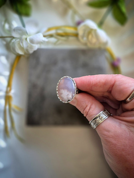 Hand holding a pinkish ring with a decorative background