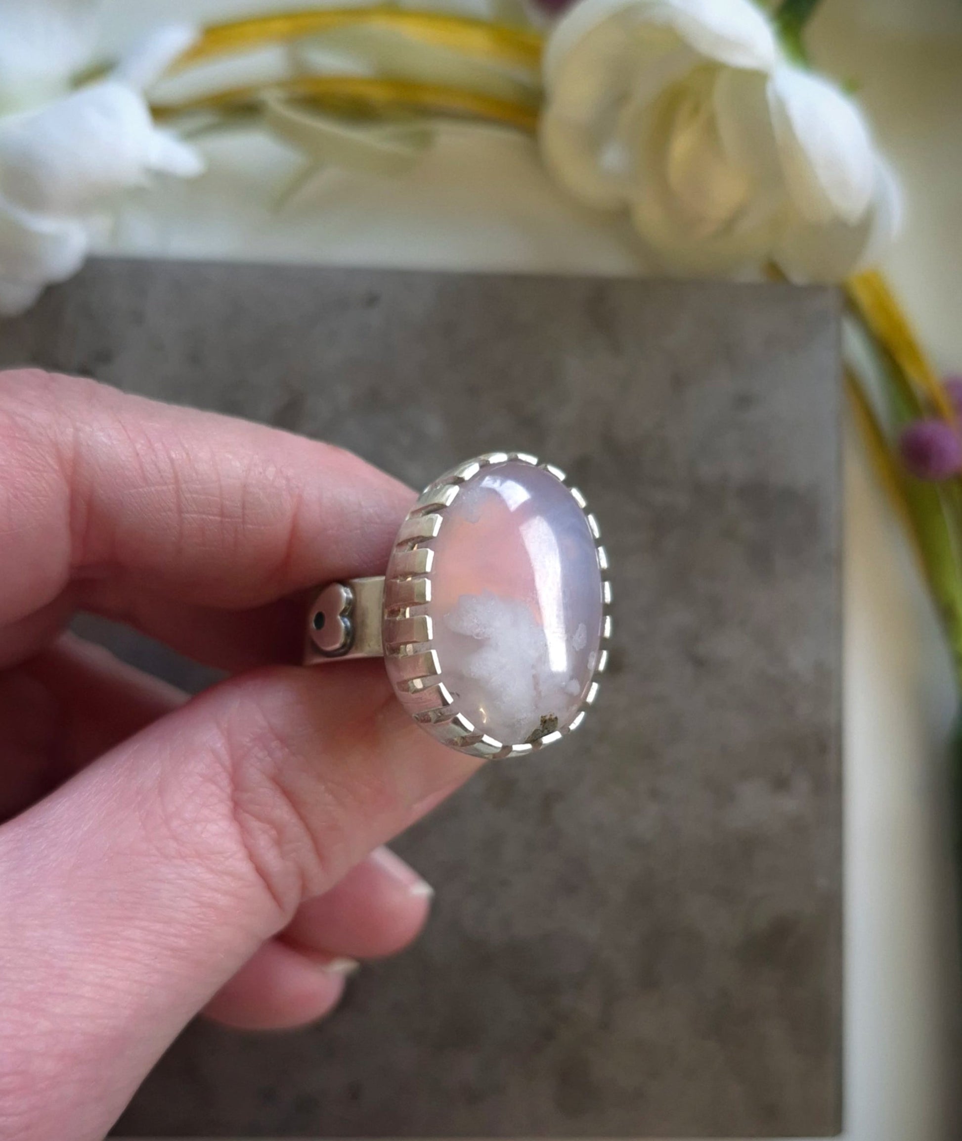 Hand holding a ring with a opaque lavender agate gemstone against a neutral background