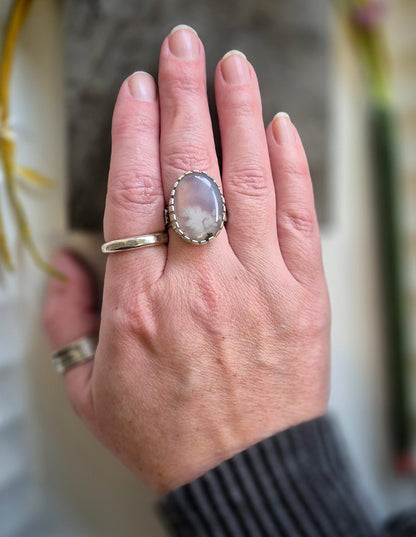 Hand wearing a ring with a large lavender agate gemstone, blurred background